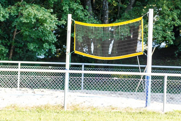 Outdoor badminton net set up in a garden or park with the net strung between two metal poles on grass and sand