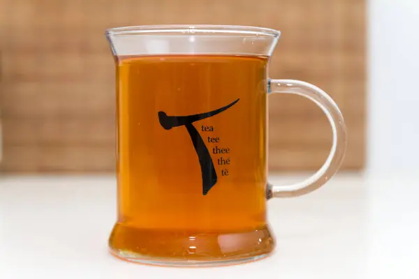 お茶のカップの静かな生活を閉じる シンボルとWord Teaのさまざまな翻訳でクリアマグの醸造されたハーブティーのホットカップ ホワイトカウンター — ストック写真