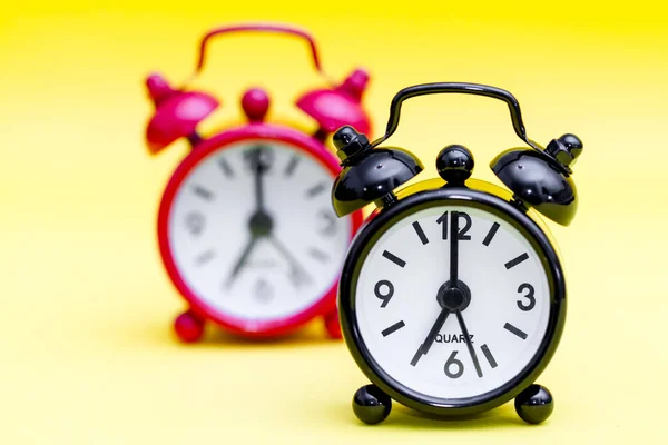 Two retro alarm clocks on yellow background displaying seven o\'clock.