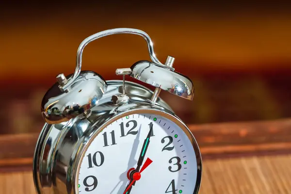 Retro silver alarm clock showing time as seven o\'clock.