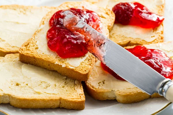 Toasted bread butter and jam on plate.