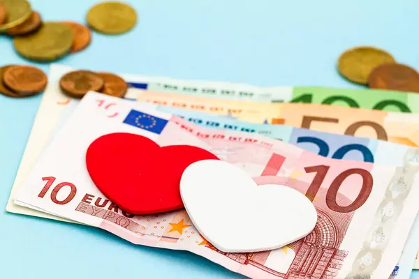 背景にコインとヨーロッパの紙幣の山に2つの装飾的な愛の心 ストックフォト