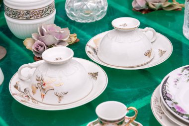 Süsleri, fincanları ve tabakları yeşil arka planda olan bir antikacıda çeşitli klasik porselenler.
