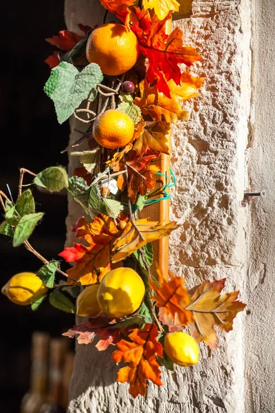 Strand of fall leave, lemons and oranges hanging on side of building in sunshine.