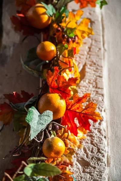 Strand of fall leave, lemons and oranges hanging on side of building in sunshine.