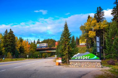 Jasper, Alberta, Kanada - 24 Eylül 2021: Jasper köyüne hoş geldiniz işareti Jasper Ulusal Parkı 'ndaki Canadian Rockies' in arka planında bir yük treniyle.