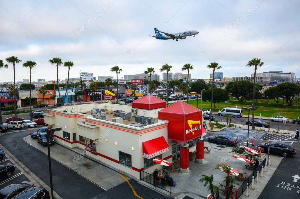 Los Angeles, California, USA - May 26, 2022 : Alaska Airlines aircraft flying above a vintage In-N-Out Burger restaurant while landing at the Los Angeles International Airport LAX.