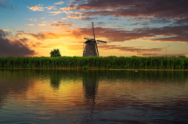 Hollanda 'daki Kinderdijk nehrinin kıyısındaki eski bir yel değirmeninin üzerinde renkli bir gün batımı. Bu 19 yel değirmeninden oluşan sistem 1740 'larda inşa edildi ve UNESCO' nun mirası haline geldi..