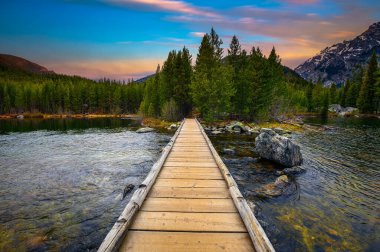 Sunset over Taggart Lake and Grand Teton Mountains in Wyoming, USA, with a footbridge in the foreground.
