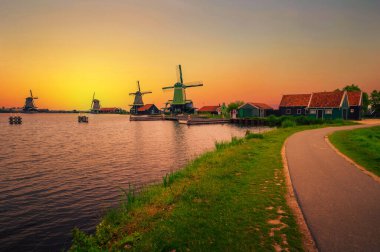 Hollanda 'nın Amsterdam yakınlarındaki Zaanse Schans Hollanda köyünde tarihi çiftlik evleri ve yel değirmenlerinin üzerinde gün batımı.