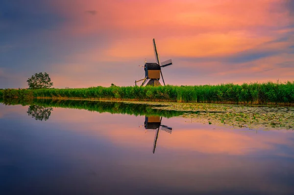 荷兰Kinderdijk的一条河边一座破旧的弯弯曲曲风车上 夕阳西下 色彩斑斓 这个由19个风车组成的系统建于1740年左右 是联合国教科文组织的一个遗址 — 图库照片