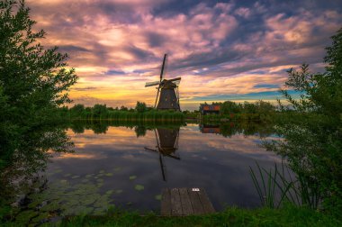 Hollanda 'nın başkenti Kinderdijk' te eski bir yel değirmeni ve akan bir nehir üzerinde renkli bir gün batımı..