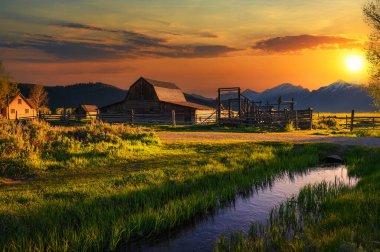 Güneşli bir yaz gününde, Grand Teton Ulusal Parkı 'nda Mormon Row' daki tarihi John Moulton Barn üzerinde renkli bir günbatımı..