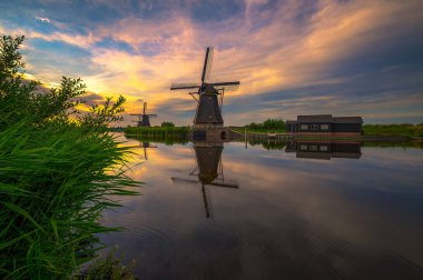 Hollanda 'nın başkenti Kinderdijk' te eski bir yel değirmeni ve akan bir nehir üzerinde renkli bir gün batımı..