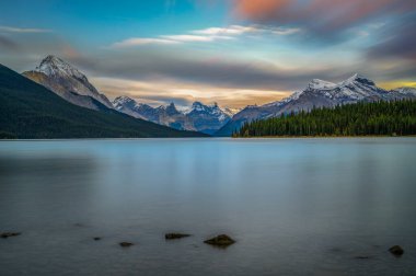 Kanada Jasper Ulusal Parkı 'nda Maligne Gölü' nün üzerinde gün batımı var. Arka planda Kanada Rocky Dağları 'nın karla kaplı zirveleri var. Uzun pozlama.