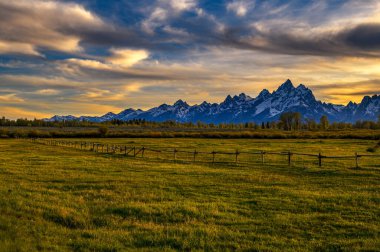 Colorful sunset above the Grand Teton mountains in Wyoming with a wooden fence in the foreground.