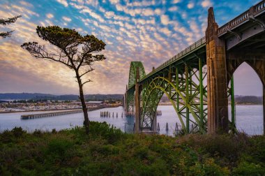 Sunset over Yaquina Bay Bridge in Newport, Oregon with cloudy sky. The Yaquina Bay Bridge is an elegant art deco structure arching over the picturesque bay. clipart