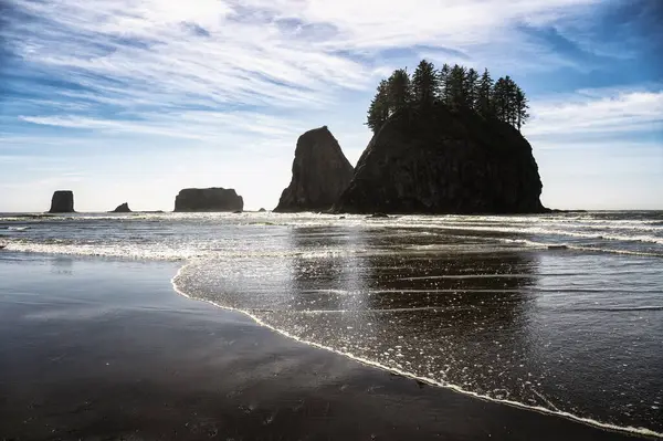 stock image Silhouetted sea stacks with trees atop on Second Beach, La Push with sparkling reflections known as a glitter pattern and dynamic sky in Washington State, photographed against the sun.