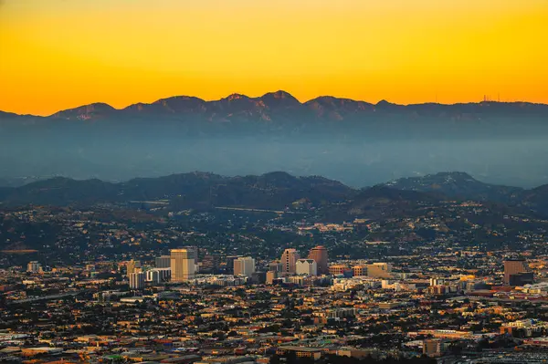 从加州洛杉矶附近的格里菲斯公园俯瞰的格伦代尔市中心和圣加布里埃尔山脉上空的日落 图库图片