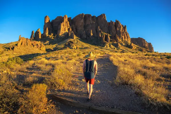 亚利桑那州落脚的荷兰人州立公园 戴着草帽的徒步旅行者走向名为迷信山脉的岩石群 免版税图库图片
