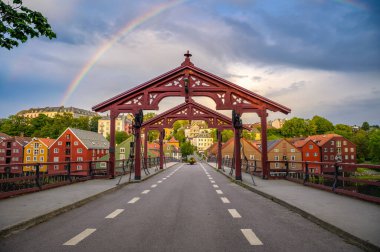 Norveç 'in Trondheim kentindeki Gamle Bybro Köprüsü, renkli ahşap evler ve arka planda gün batımında çekilmiş gökkuşağı ile Nidelva Nehri' ni geçiyor..