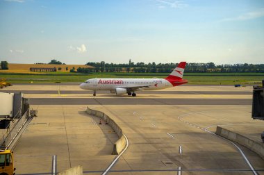 Viyana, Avusturya - 26 Haziran 2024: Avusturya Havayolları Airbus A320 Viyana Uluslararası Havalimanı 'nda arka planda açık alanlarla taksicilik yapıyor.
