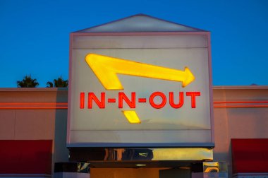 Los Angeles, Kaliforniya, ABD - 03 Kasım 2023: Günbatımında bir binanın dış tarafında sarı ok ve kırmızı metin ile aydınlatılmış In-N-Out Burger tabelası.