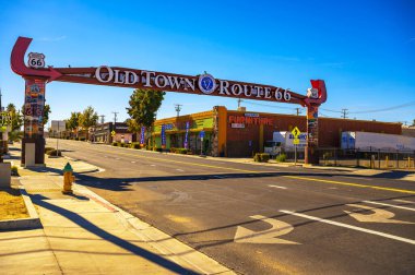 Victorville, Kaliforniya, ABD - 3 Kasım 2023 Vibrant sokak sahnesi Victorville 'deki Old Town Route 66 neon kemer yolu tabelasının altında, açık mavi bir gökyüzü ve klasik yol kenarı eğlenceleriyle.
