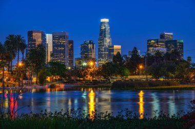 Los Angeles şehir merkezinin gece manzarası Echo Park 'tan gökdelenlerin, palmiye ağaçlarının ve gölün yansımalarının yer aldığı gökyüzü..