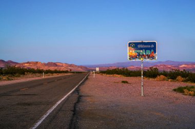 Ölüm Vadisi, Nevada, ABD - 11 Kasım 2023: Ölüm Vadisi Ulusal Parkı 'nda gün batımında çekilmiş bir çöl manzarasına karşı hazırlanmış renkli çıkartmalı Nevada yol tabelasına hoş geldiniz.