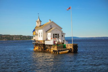 Oslofjord, Norveç - 31 Temmuz 2024: Dyna Fyr Deniz Feneri Oslo kenti yakınlarındaki küçük bir adada, şimdi bir restoran olarak hizmet veren, gün ışığının sıcak renkleriyle aydınlatılan.