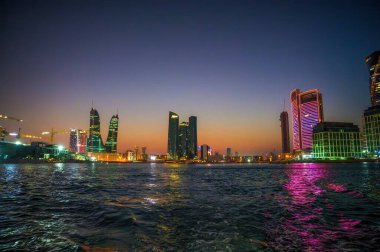 Manama, Bahreyn - 27 Aralık 2023: Conrad Bahreyn Finans Limanı, Rotana Hotel Bahreyn Kempinski ve Hotel Kempinski ile suya yansıyan modern tatil beldelerinin gece görüntüsü.