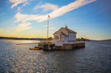 Oslofjord, Norveç - 31 Temmuz 2024: Dyna Fyr Deniz feneri Oslo kenti yakınlarındaki küçük bir adada, günbatımının sıcak renkleriyle aydınlatılmış bir restoran olarak hizmet vermektedir..