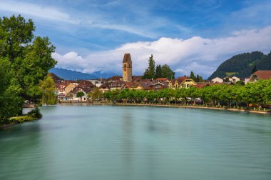 İsviçre 'nin Interlaken kentinin arka planında Aare Nehri ve İsviçre Alpleri' nin yer aldığı manzarada geleneksel binalar ve yemyeşil alanlar bulunuyor. Uzun pozlama.