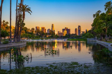 Los Angeles şehir merkezinin günbatımı manzarası Echo Park Gölü 'nden yükseliyor palmiye ağaçları ve suda yüzen teknelerle..