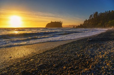 Ruby Sahili 'nde Pasifik Okyanusu' nun üzerinde renkli bir günbatımı dalgalar ve Washington eyaletindeki Olimpiyat Ulusal Parkı 'nda kayalık bir kıyı şeridi.