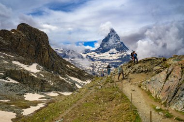 Zermatt, İsviçre - 01 Temmuz 2024: İsviçre 'de karla kaplı Matterhorn manzaralı bir grup turist dağ yolunda