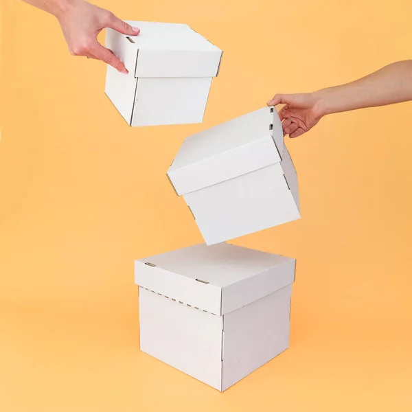 Eller, turuncu arka planda farklı boyutlarda beyaz el işi kutuları tutar. Mesaj ve logo için yer. Paketleme, Padarunka, taşınma kavramı. Yüksek kalite fotoğraf