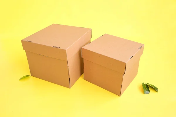 Craft boxes on a yellow background with a decor of green leaves. Place for text and logo. The concept of packaging, uniform style, holiday, gifts. High quality photo