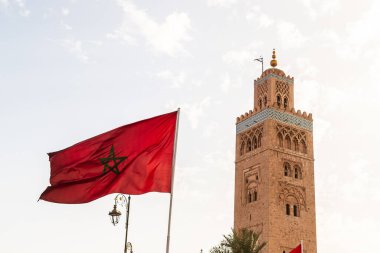 Gün boyunca Fas 'taki Marakeş Medinesi' ndeki Koutoubia Camii minaresine yakın çekim. Fas bayrağı ön planda görülebilir..