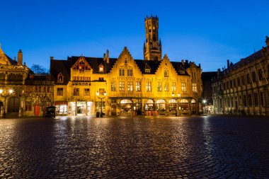 BRUGES, BELGIUM - 19 Şubat 2016: Bruges 'deki Burg Meydanı' ndaki binalar, alacakaranlıkta mavi gökyüzü ile. Bruges 'ün çan kulesi uzaktan görülebilir..