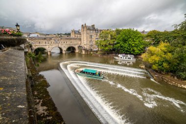 BATH, İngiltere - 12. AĞUSTOS 2023: Bath England 'daki Avon Nehri üzerindeki Pulteney Köprüsü. Bir tekne ve insanlar görülebilir..