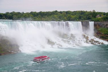 NIAGARA FALLS, CANADA - 27TH JUL 2022: A large group of people on the Niagara City Cruises boat in Niagara Falls with the American Falls in the background clipart