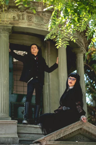 Dark gothic couple in large ancient abandoned mausoleum in neoclassical style with columns and stairs in the forest