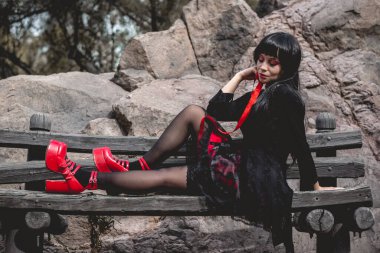 Siyah elbiseli, kırmızı platformlu, genç, seksi ve vampir gotik bir kız. Oturmuş ve 