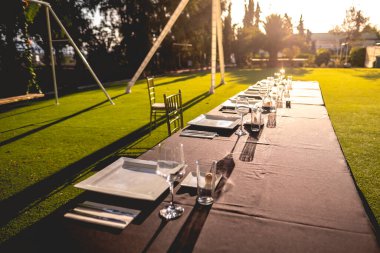 Gün batımında yeşil çimlerle çevrili bir bahçede gözlüklü ve zarif masalı merkezi düğün masası.