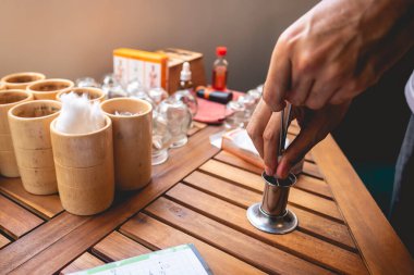 Geleneksel Çinli tıp doktoru ahşap bir masada alkolle aletleri sterilize ediyor. Cam bardaklar da bardak, otlar, pamuk, el yazısı notları ve diğer tıbbi malzemeler için.