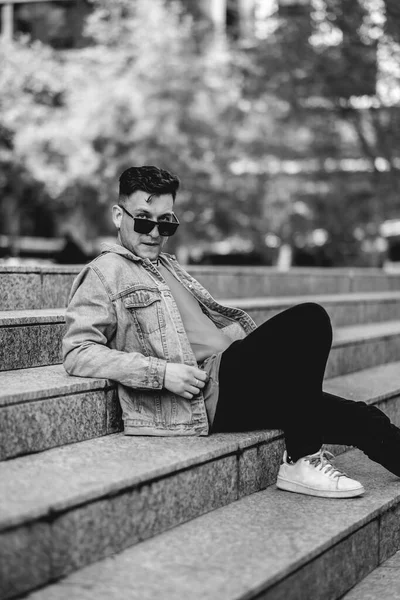 Jonge Aantrekkelijke Model Man Met Zonnebril Spijkerjasje Zwarte Jeans Zittend — Stockfoto
