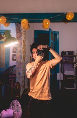 Geceleri evinde tişört giyen dövmeli bir gencin portresi.