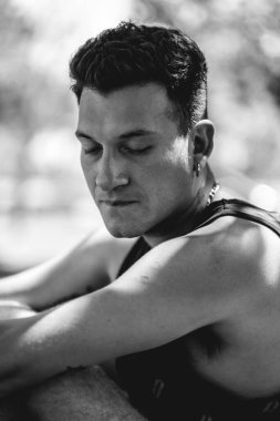 4 yapraklı yonca dövmeli, kolsuz tişörtlü, zincirli ve küpeli çekici genç bir adamın portresi.)